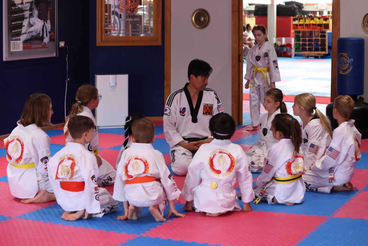Young students sitting in a circle on the dojang mats, listening to their instructor